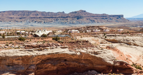 A desert landscape with unique rock formations and modern structures in the foreground, under a clear blue sky.