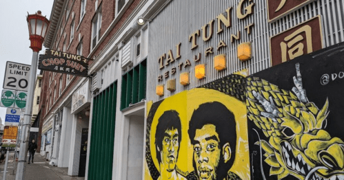 A street view of Tai Tung restaurant with vibrant mural art and a street sign indicating a speed limit of 20.
