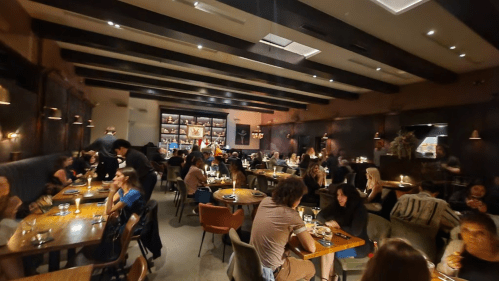 A bustling restaurant interior with diners at tables, warm lighting, and a cozy atmosphere.