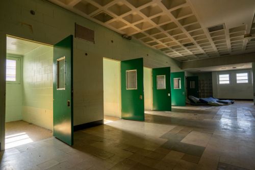Abandoned room with green doors and windows, featuring empty spaces and a mattress on the floor.