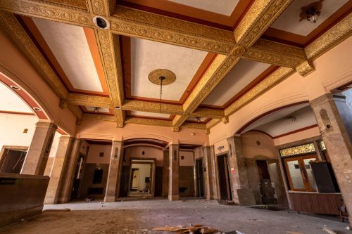 Interior of an abandoned building featuring ornate ceiling details, empty space, and scattered debris on the floor.