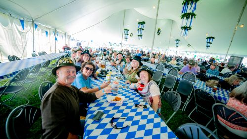 A group of people in hats enjoying drinks and snacks at a festive outdoor event under a large tent.