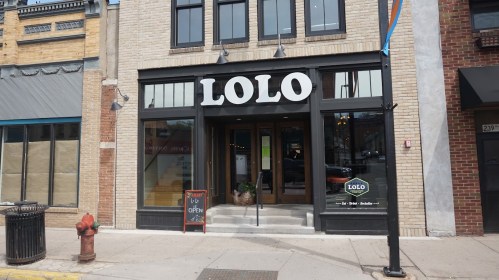 Exterior of a restaurant named "LOLO," featuring large windows and an open sign, located on a city street.