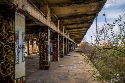 Abandoned building with graffiti-covered pillars and overgrown vegetation, under a blue sky.