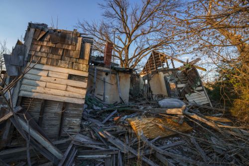 A dilapidated structure in ruins, surrounded by fallen debris and bare trees under a clear blue sky.