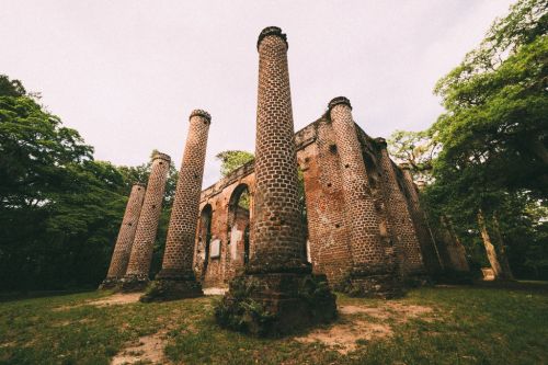 Ruins of a brick structure with tall, cylindrical columns surrounded by greenery and trees.