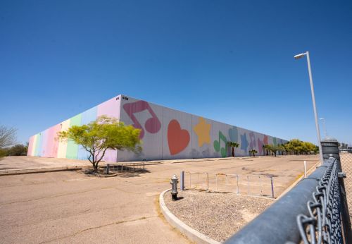 A colorful mural featuring musical notes, hearts, and stars on a large building, surrounded by a chain-link fence.