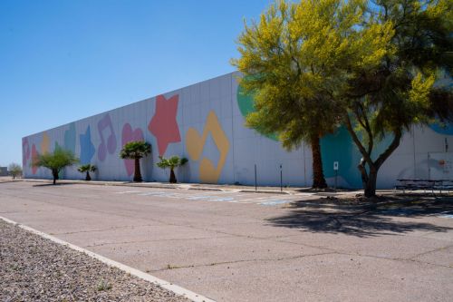Colorful geometric shapes adorn the side of a large building, surrounded by palm trees and a clear blue sky.