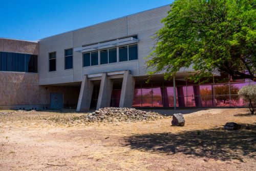 Modern building with large windows, a sloped entrance, and a rocky landscape under a clear blue sky.