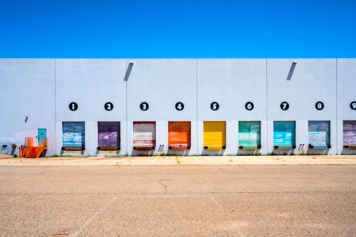 Colorful loading dock doors numbered 1 to 8 on a light gray building against a clear blue sky.
