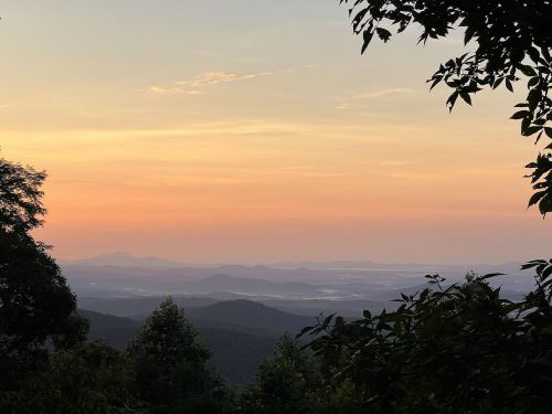 A serene mountain landscape at sunset, with layers of hills and a colorful sky in soft hues of orange and pink.