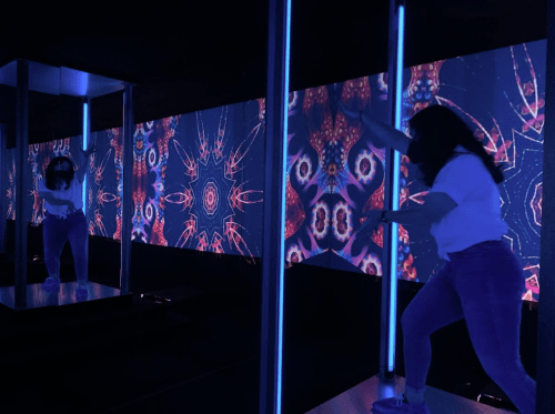 A person dances near a pole in a dark room with vibrant, colorful projections on the walls.