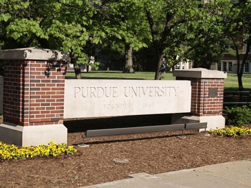 Sign for Purdue University, featuring the name and founding year, surrounded by greenery and flowers.