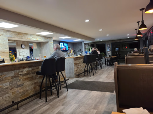 A cozy bar area with stone walls, featuring a few patrons seated at the counter and tables in a warm, inviting atmosphere.
