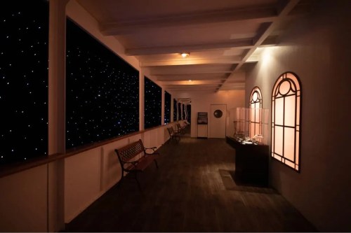 A dimly lit corridor with benches and windows, revealing a starry night sky outside.