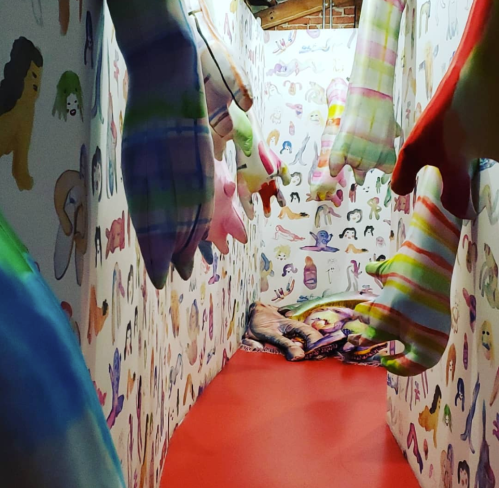 A colorful, whimsical hallway with oversized, patterned hands and walls covered in playful illustrations.