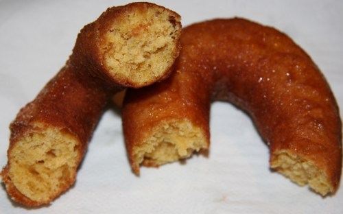 Two golden-brown, curved pastries with a shiny glaze, one partially bitten, resting on a white surface.