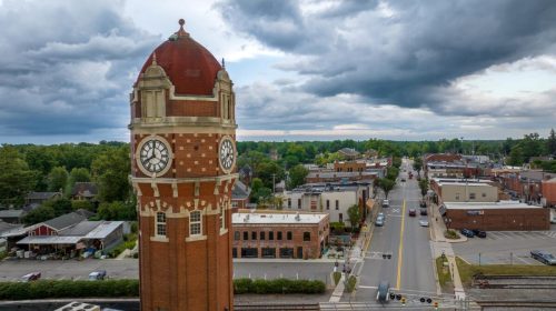 A clock tower stands tall over a small town, with streets lined by buildings and a cloudy sky above.