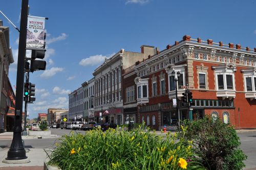 A vibrant downtown scene featuring historic buildings, traffic lights, and blooming flowers under a clear blue sky.