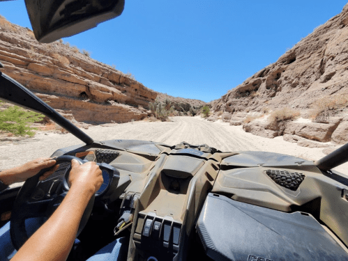 View from an ATV driving through a rocky canyon with clear blue skies above. Hands on the steering wheel.
