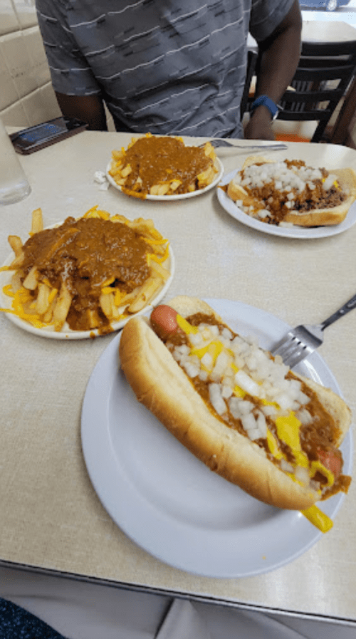 A table with two plates of chili cheese fries and a hot dog topped with mustard and onions.