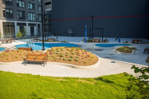 A landscaped courtyard featuring pools, benches, and greenery, surrounded by modern buildings.