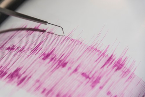 A close-up of a seismograph displaying purple seismic wave patterns, with a pen-like tool touching the graph.