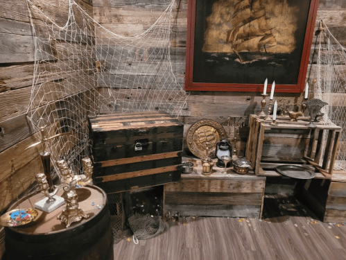 A rustic corner with wooden crates, a ship painting, candles, and decorative items, evoking a nautical theme.