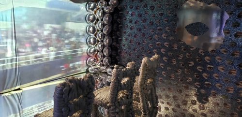 A unique interior space featuring textured walls and a chair, with a view of a crowd through a large opening.