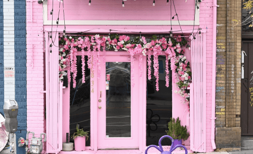 A vibrant pink storefront adorned with floral decorations and string lights, creating a cheerful atmosphere.