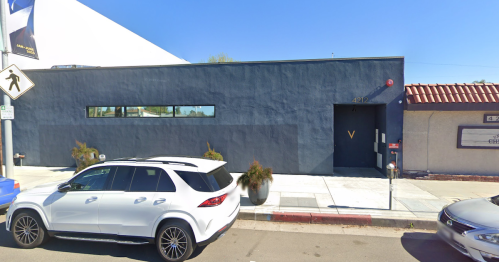 A modern, dark blue building with a red roof, parked white SUV in front, and minimal landscaping.
