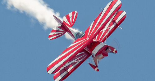 A red and white biplane performs a stunt in the sky, leaving a trail of smoke behind.