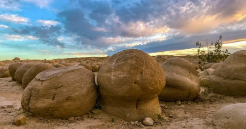 Boulders with rounded shapes scattered across a desert landscape under a colorful sky at sunset.