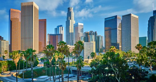 A vibrant city skyline featuring tall buildings and palm trees under a clear blue sky.