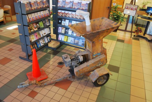 An old, rusty machine with a funnel-shaped top, next to a traffic cone, in a tiled lobby area.