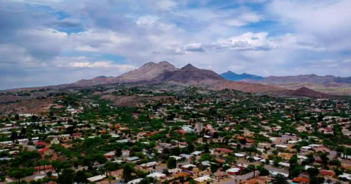 Aerial view of a mountainous landscape with a town nestled in a green valley under a cloudy sky.