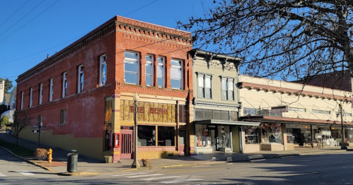 Historic buildings line a sunny street, showcasing brick and wooden architecture in a quaint town.
