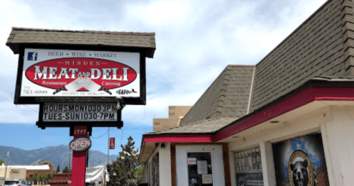 Sign for Minden Meat and Deli, featuring a restaurant and market, with a clear blue sky in the background.