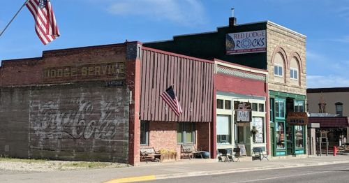 Historic buildings with storefronts, American flags, and a Coca-Cola mural in a small town setting.