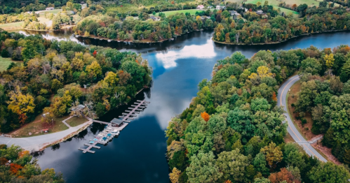 Aerial view of a serene river surrounded by lush greenery and a small marina, with a winding road nearby.