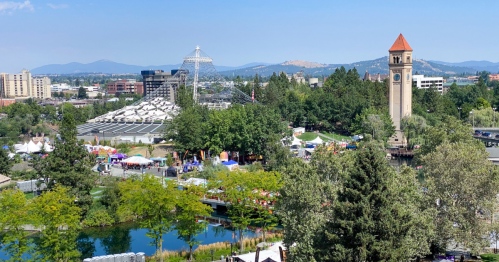 A scenic view of a park with a clock tower, trees, and festival tents under a clear blue sky.