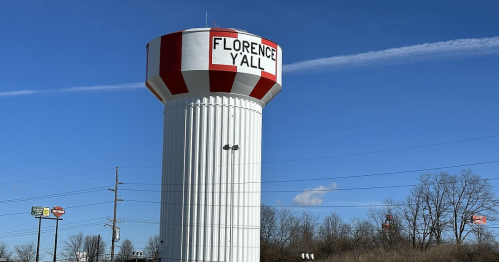 A tall water tower with red and white stripes, featuring the text "FLORENCE Y'ALL" against a clear blue sky.