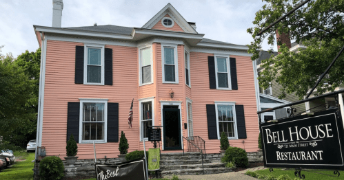 A pink Victorian-style house with black shutters, featuring a sign for Bell House Restaurant in front.