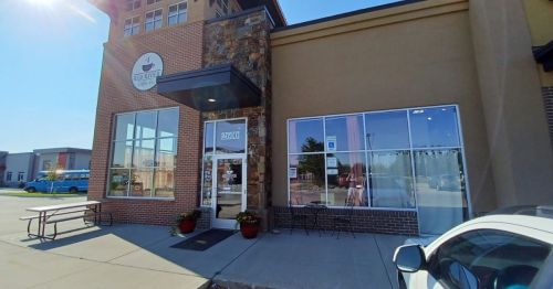 Exterior view of a coffee shop with a stone facade, large windows, and a welcoming entrance on a sunny day.