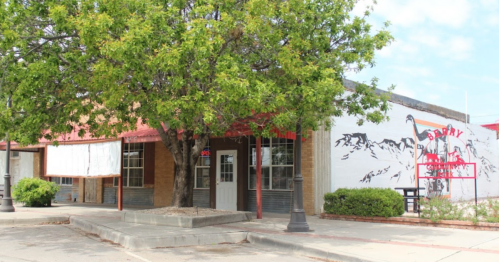 A small building with a red awning, surrounded by greenery and featuring a mural of mountains on the side.