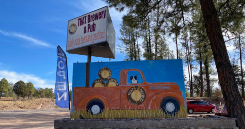 A colorful mural of an orange truck with a dog, next to a sign for THAT Brewery & Pub in a wooded area.