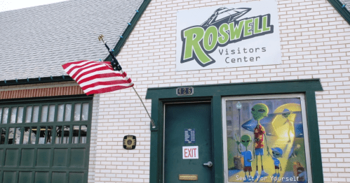 Exterior of the Roswell Visitors Center featuring an American flag and a window display with alien figures.