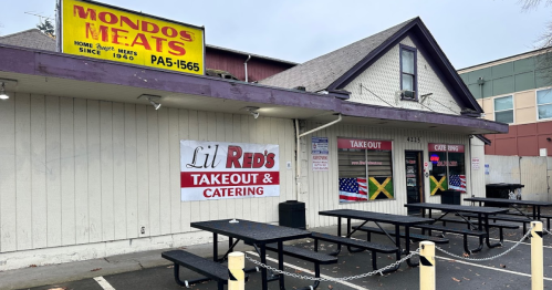 Exterior of Lil Red's Takeout & Catering with picnic tables, featuring a sign for Mondos Meats above.