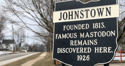 Sign for Johnstown, founded in 1813, noting famous mastodon remains discovered in 1926. Trees and road in background.