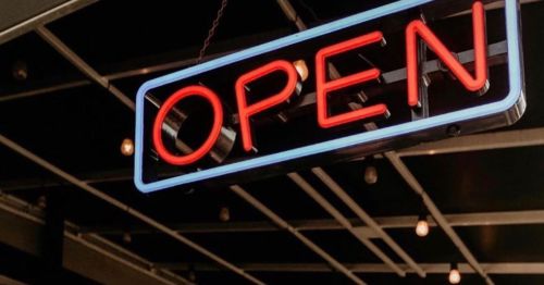 A glowing neon "OPEN" sign hanging in a modern storefront, with warm lights in the background.